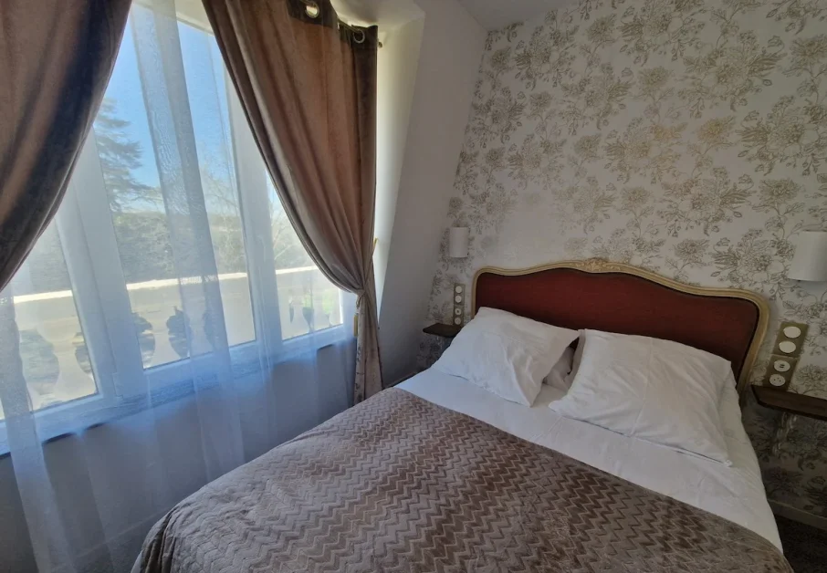 Chambre Douillette 1 Notre modèle de chambre douillette et lumineuse d'inspiration rétro avec vue sur le parc et mobilier vintage. Tapisserie motif floral délicat