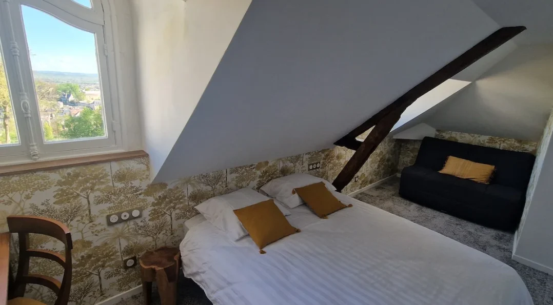 Notre modèle de chambre quadruple au château avec vue sur le parc, lit double + canapé-lit, mobilier vintage et tapisserie motif ancien. Ici pièce en soupente
